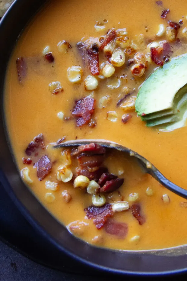 Close up of a spoon scooping a bite of the butternut squash and sweet potato soup with corn and bacon garnish.