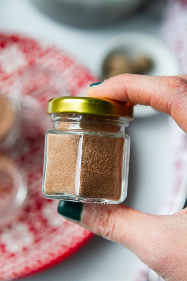 Fingers holding a little jar of cinnamon sugar blend.