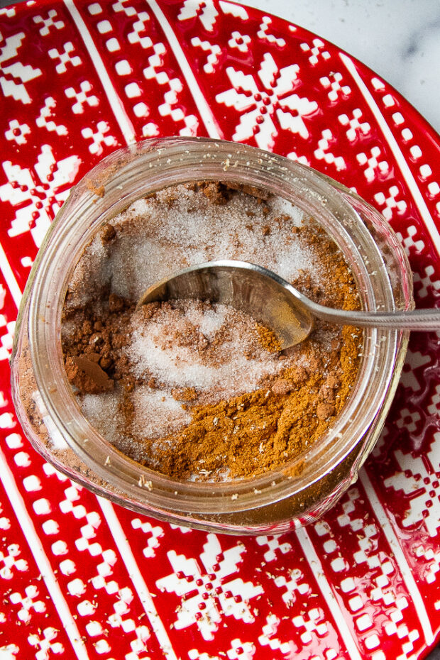 A small mason jar with the ingredients for cocoa cinnamon sugar being stirred.