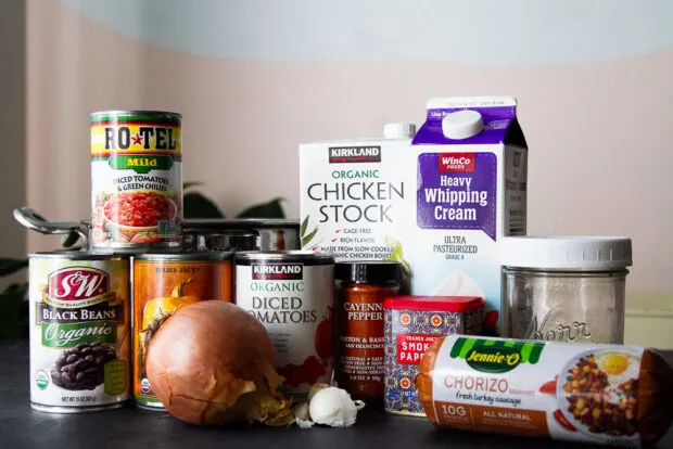 Ingredients displayed for pumpkin chorizo chili -- black beans, Rotel tomatoes, pumpkin puree, diced tomatoes, chicken stock, garlic, heavy cream, cumin, and chorizo.