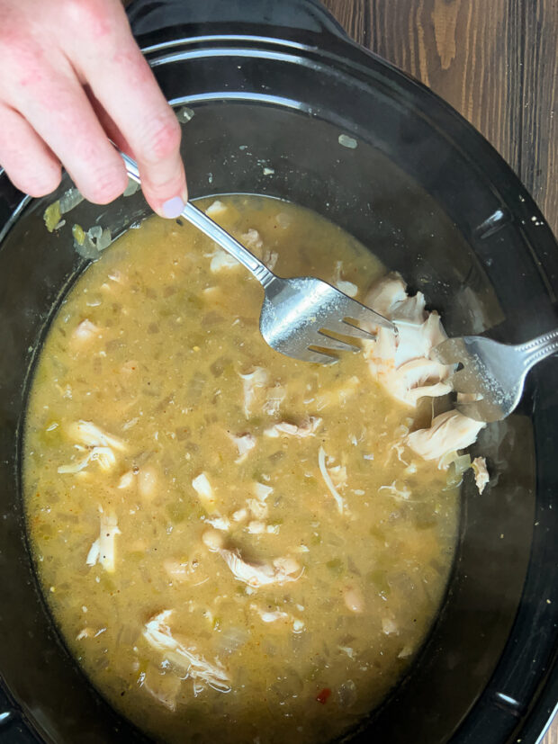 Cooked chili in crock pot and chicken is being shredded.