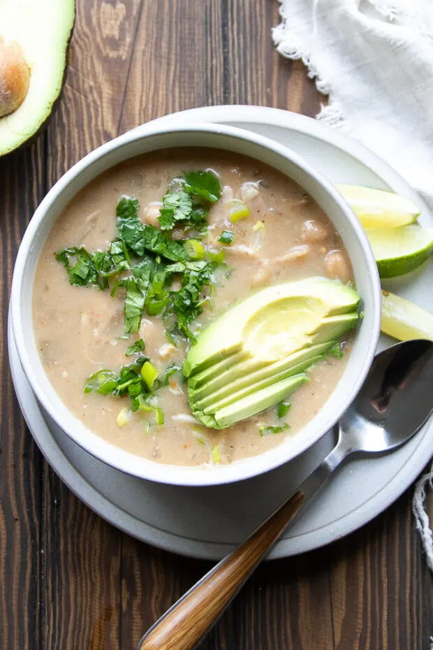 Gray bowl with white chicken chili topped with sliced avocado and fresh cilantro.