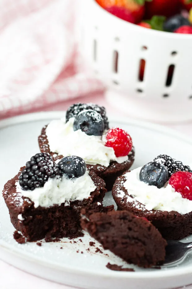 Three flourless chocolate cakes on a plate dressed with whipped cream and berries. 