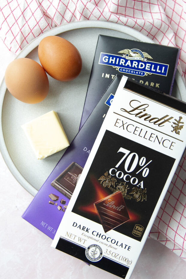 Ingredients for flourless chocolate cake on a plate: 70% dark chocolate bars, eggs, and butter.