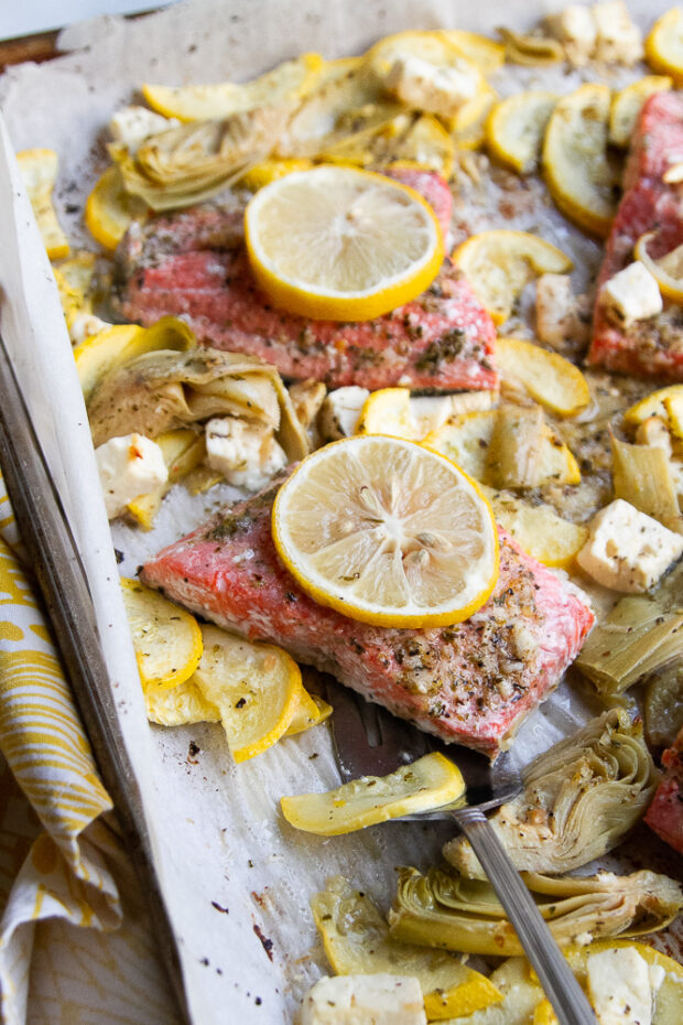 Baked Mediterranean Salmon, yellow squash, artichoke hearts, and feta on a large parchment lined baking sheet.