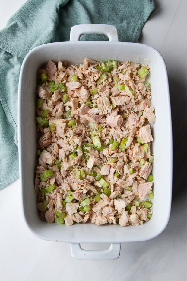 White casserole dish with crumbled tuna and celery pieces.