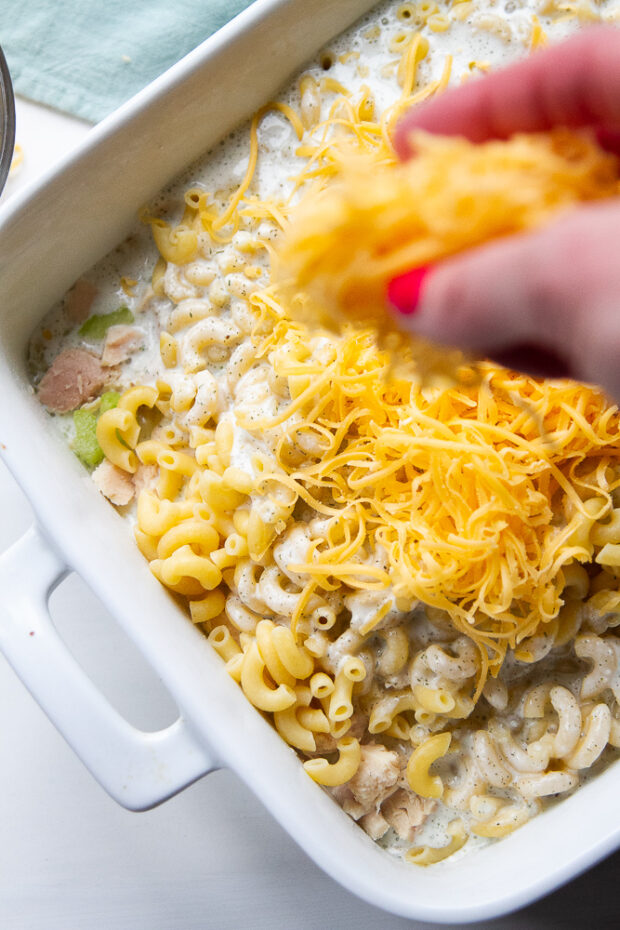 Sprinkling shredded cheese over the pasta in the casserole dish.