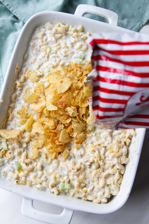 Sprinkling crushed potato chips over the tuna casserole.