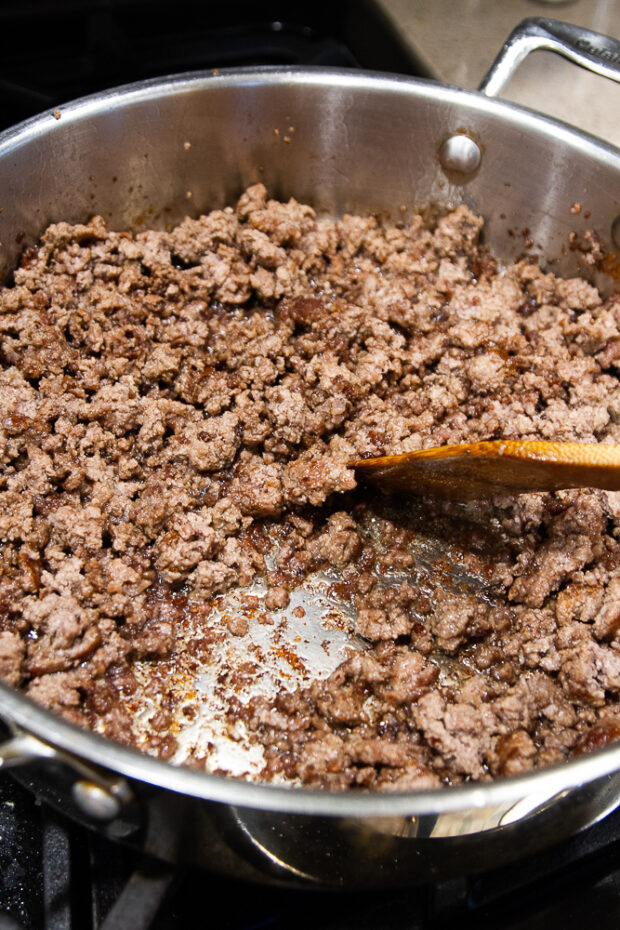 Ground beef cooked in a large stainless skillet. The beef has bits of crispy edges.