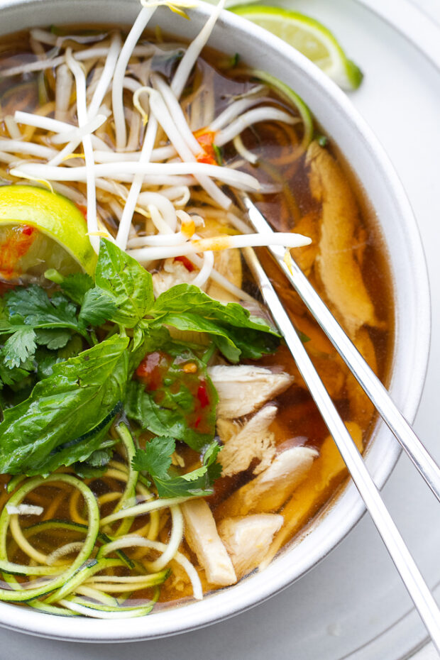 A bowl of Chicken Pho Soup with garnishes and a set of chopsticks in the bowl with the soup. 