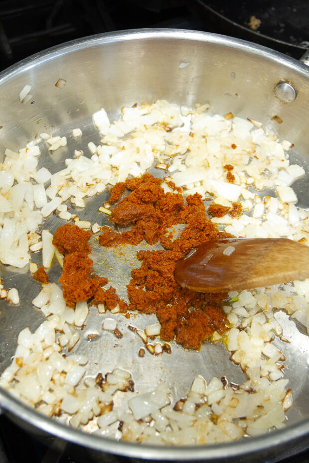 A large skillet with sautéed onions and curry paste.