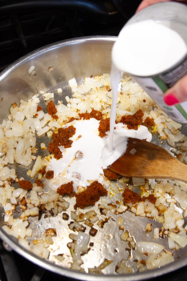 Adding coconut milk to the skillet with the onions and curry paste.