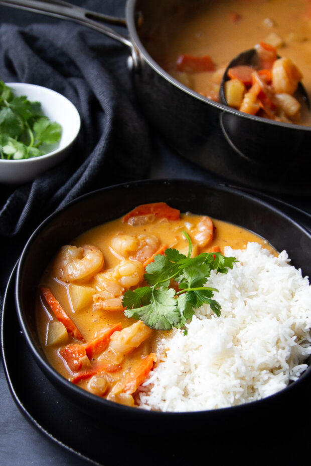 Coconut Shrimp Curry in a black bowl with some steamed jasmine rice and fresh cilantro.