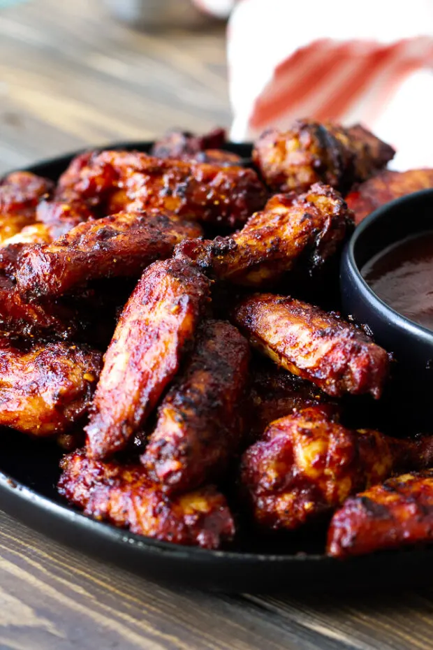 A plate of smoked chicken wings with a small bowl of BBQ sauce.