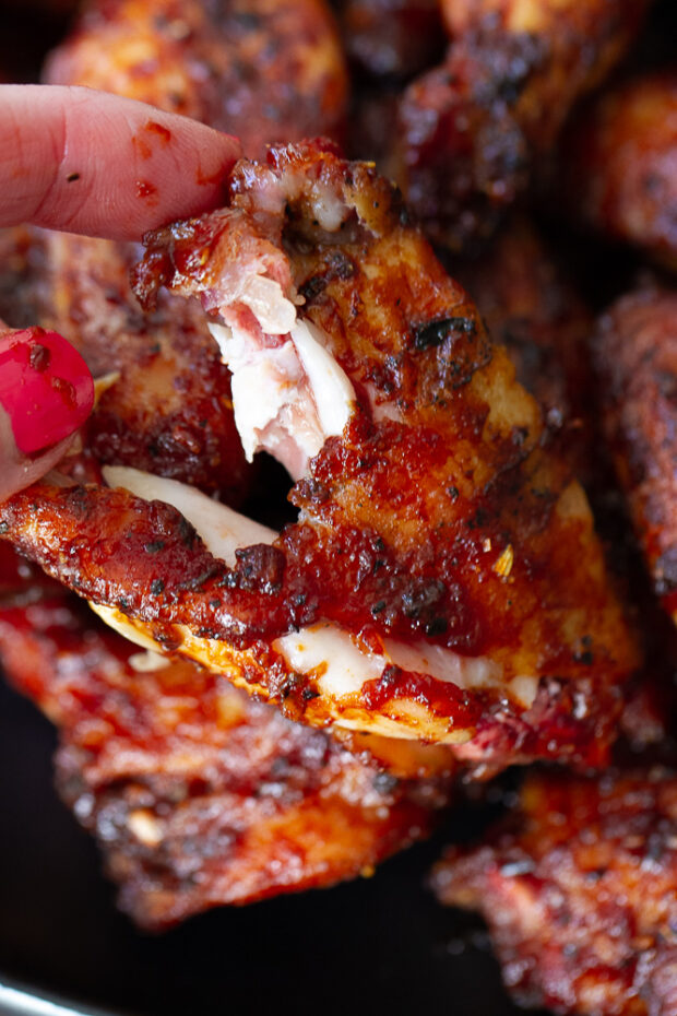 A BBQ smoked chicken wing that has been pulled apart so you can see the moist pieces of meat inside and the crispy, caramelized skin.