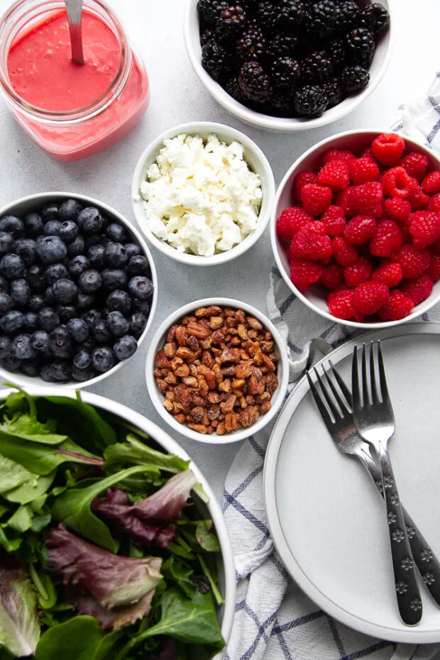 Ingredients for this berry spring green salad: spring mix salad greens, candied nuts, blueberries, raspberries, blackberries, goat cheese, and raspberry vinaigrette.