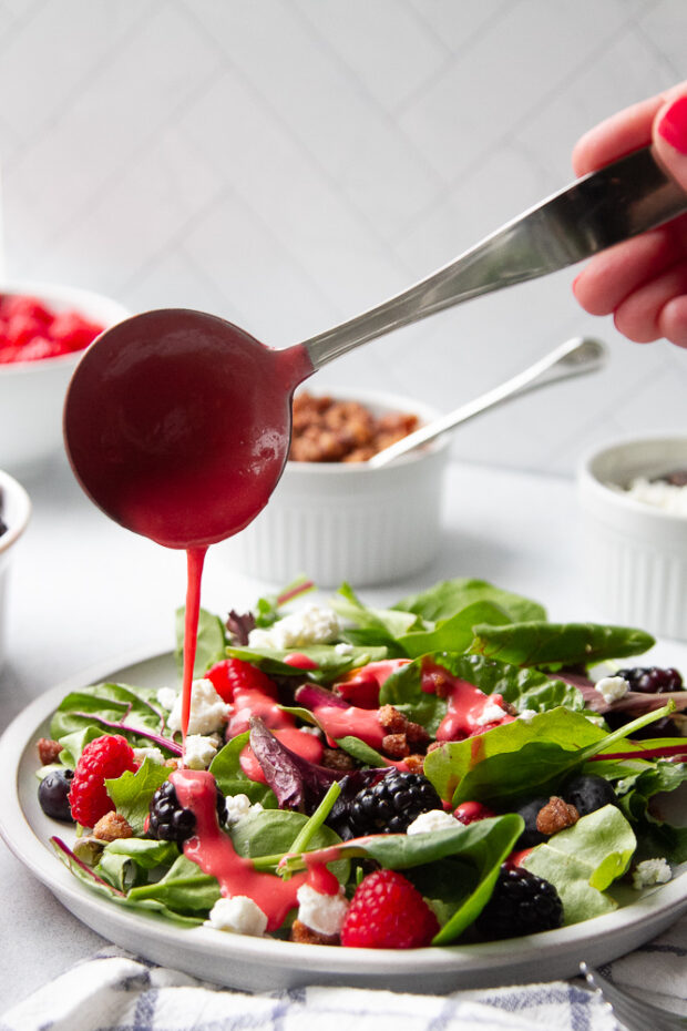 Raspberry vinaigrette being poured over the berry salad.