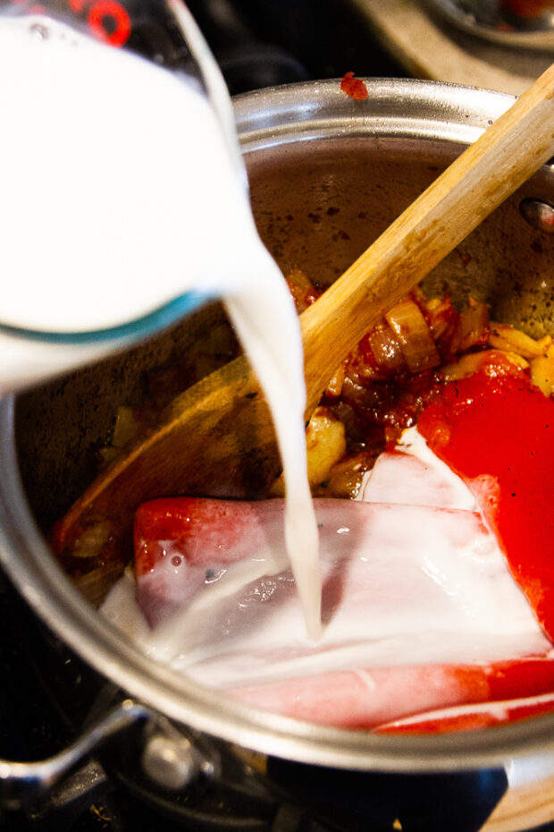 Adding milk to the saucepan along with the red peppers and tomato paste.