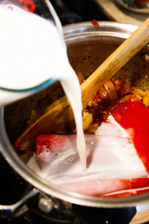 Adding milk to the saucepan along with the red peppers and tomato paste.