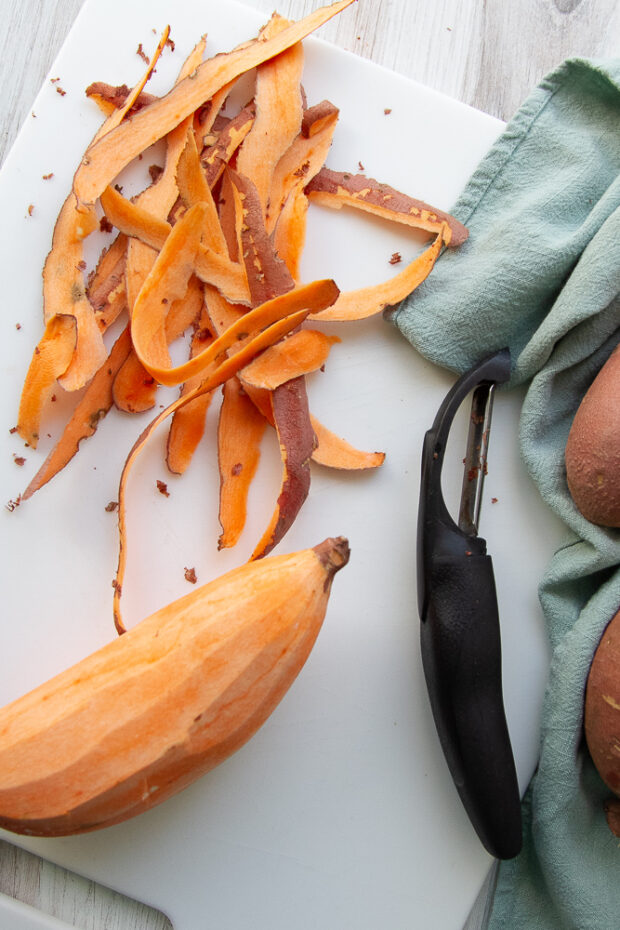 Sweet potato that has been peeled. the peels are sitting on the cutting board.