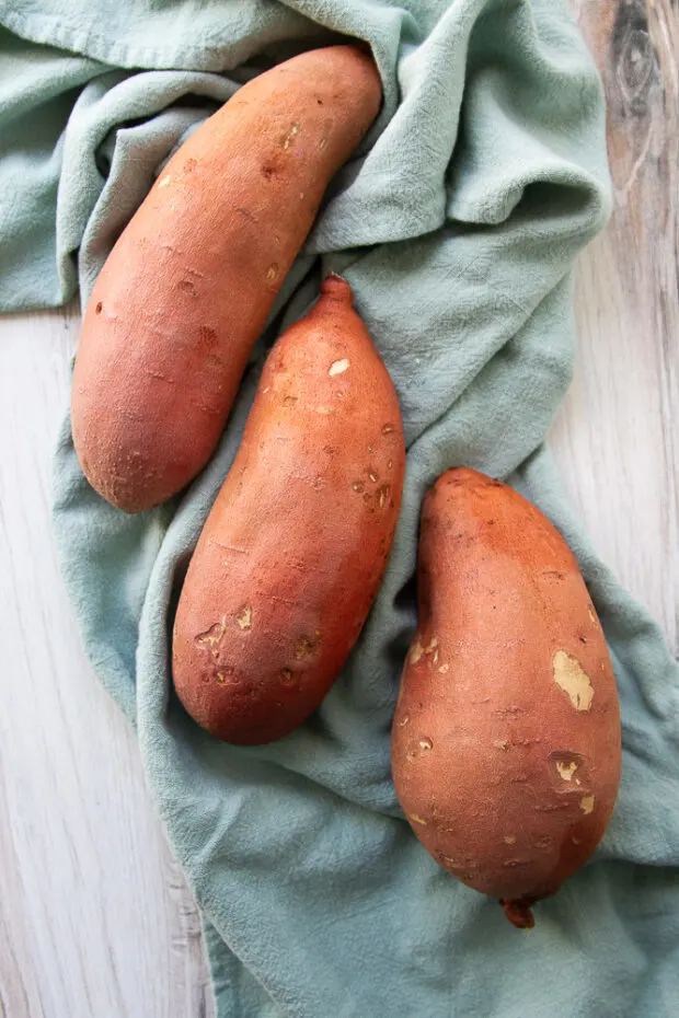 Three sweet potatoes on an aqua kitchen towel. 