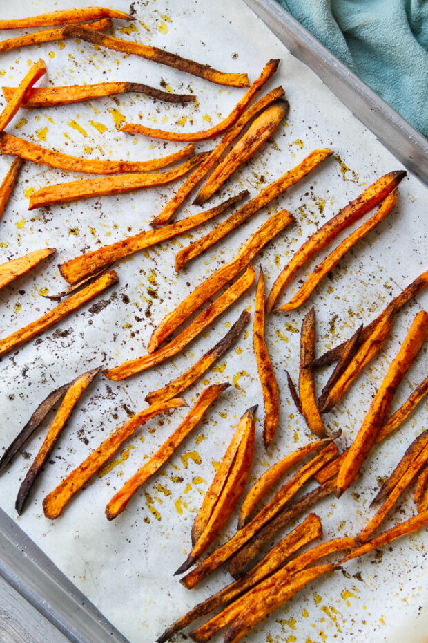 Roasted sweet potato fries on a parchment lined sheet pan.
