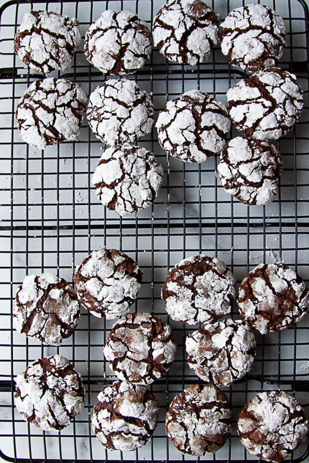 Comparison between rolling dough balls in granulated sugar before powdered sugar. The top ones have been rolled in granulated sugar and the powdered sugar is whiter. The sugar on the other cookies have dissolved into the dough in spots.