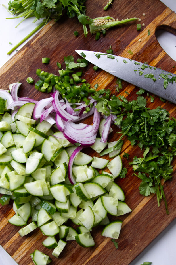 Chopped cokes, onion, cilantro, and jalapeño on a cutting board.