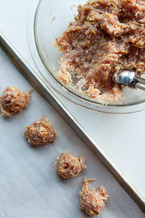 Meatballs being scooped out onto a parchment baking sheet.