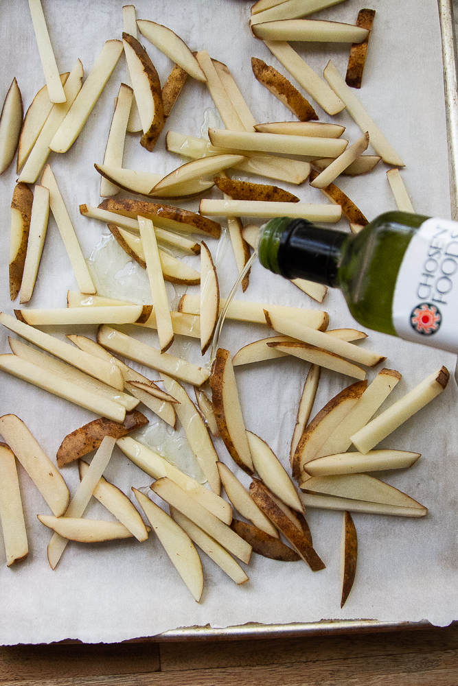 Raw potatoes cut into fries on a sheet pan drizzled with avocado oil.