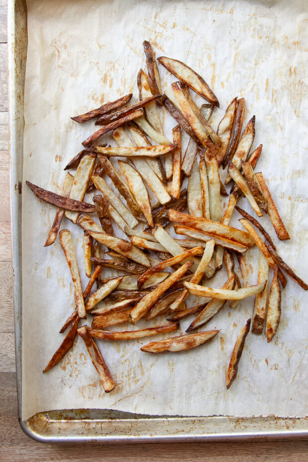Oven fries on a sheet pan pushed together to the middle of the pan.