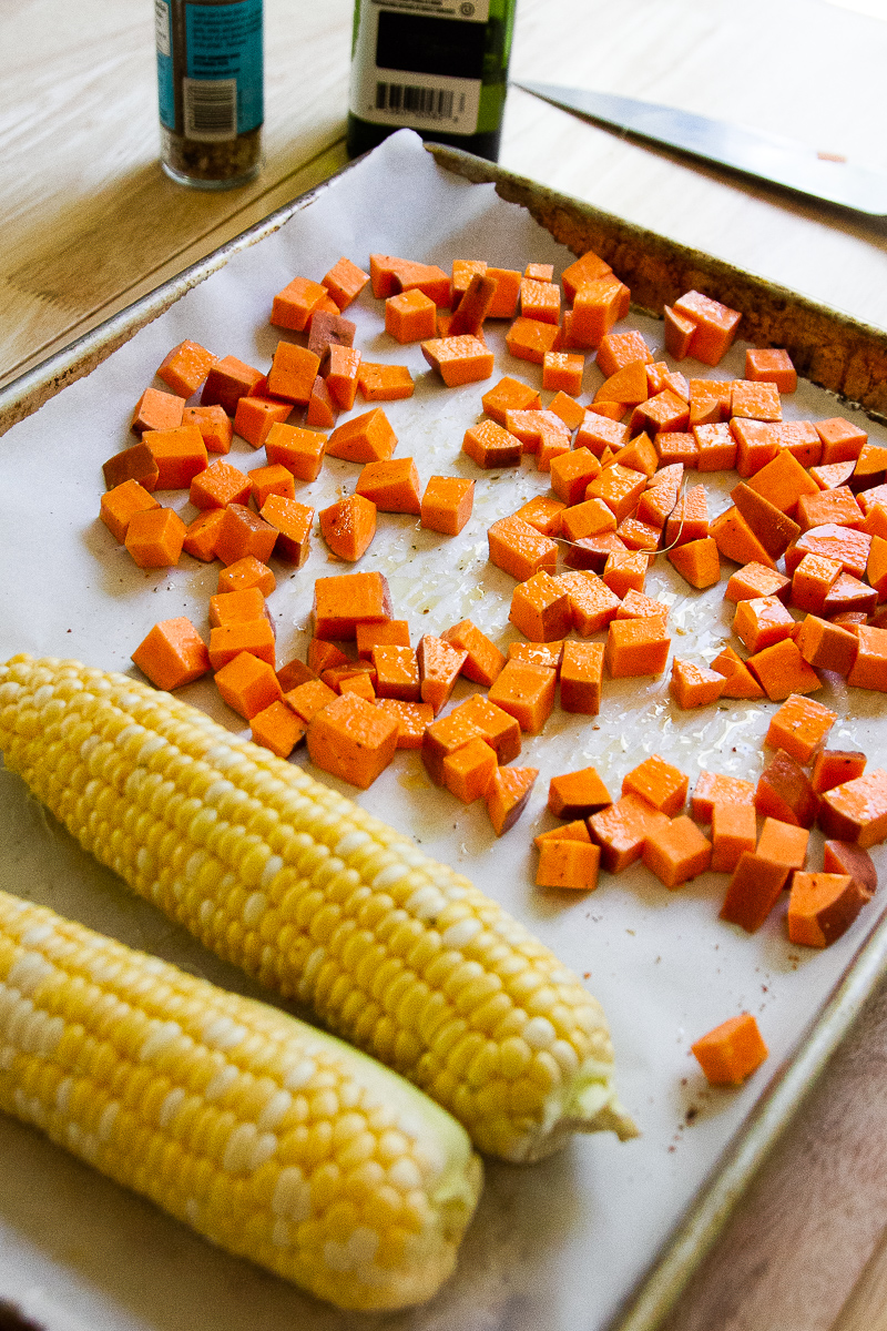 two ears of corn and some diced sweet potatoes on a sheet pan.